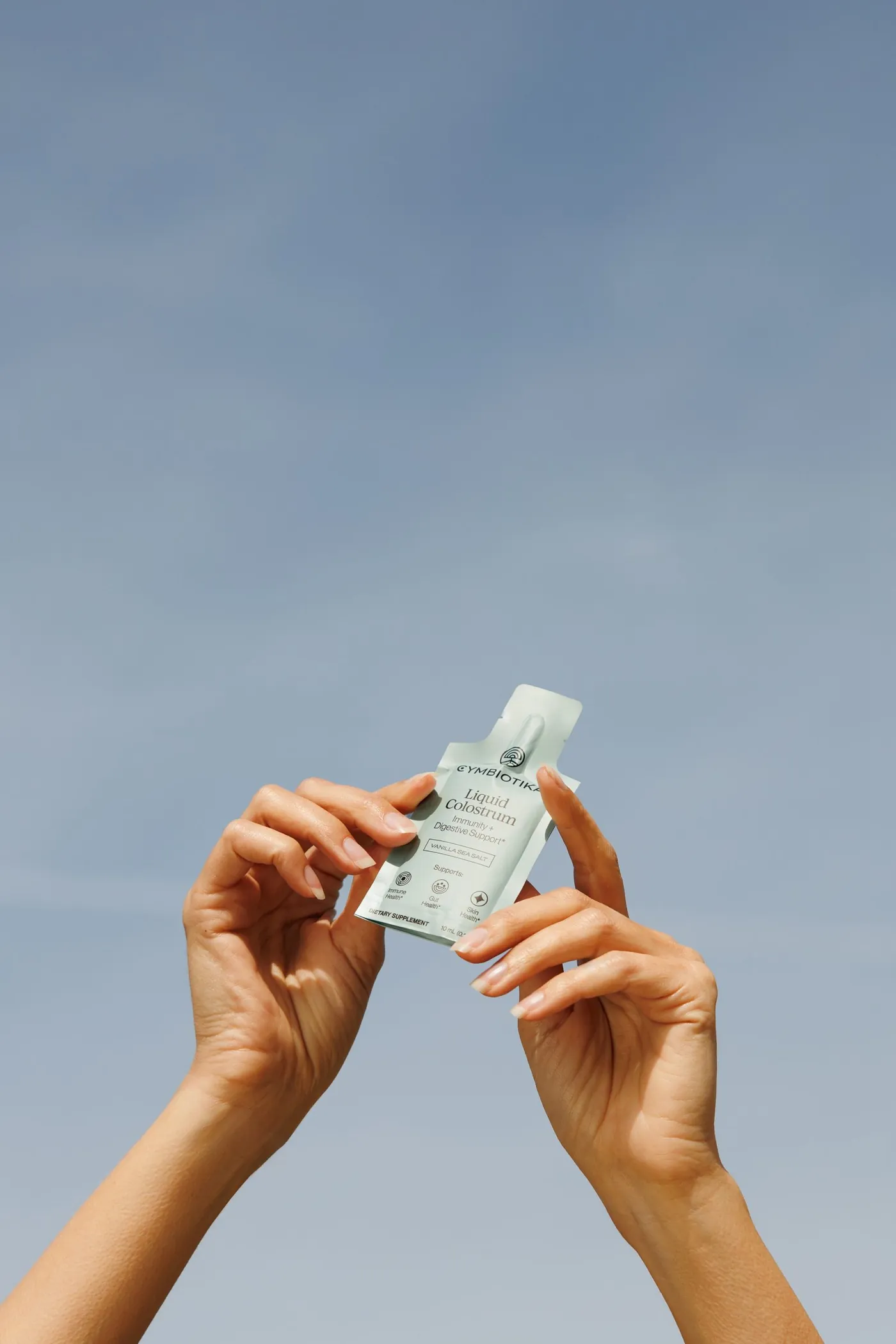 Hands holding a Colostrum packet against the sky