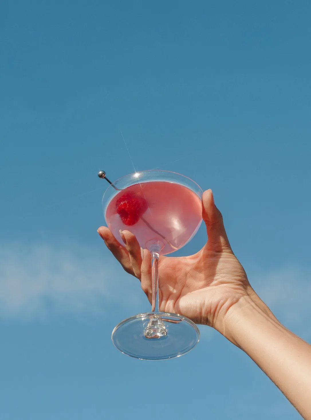 Hand raising a pink coupe against the sky